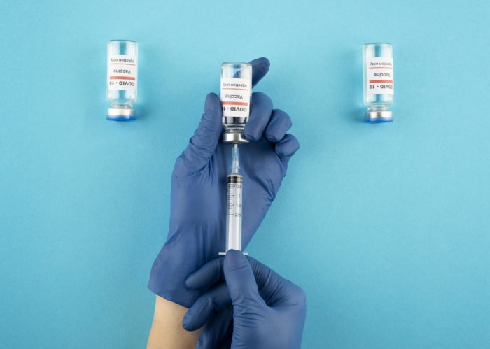 close up hand holding coronavirus vaccine 700x499 - Ketahui Varian Vaksin Corona dan Pentingnya Melakukan Vaksin