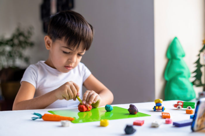 small caucasian boy playing with colored plasticine making figures white table happy child idea 700x466 - 7 Ide Permainan Anak yang Mendidik untuk Tumbuh Kembangnya